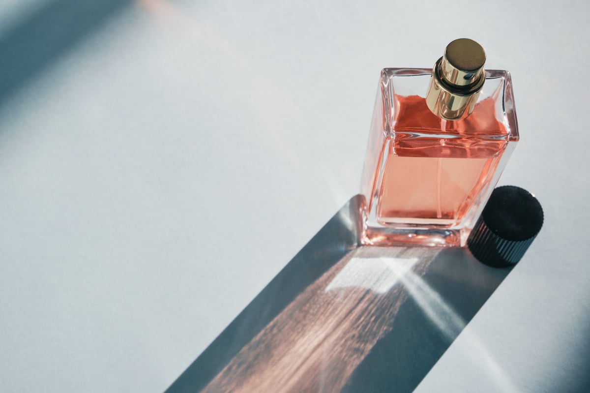 Clear glass perfume bottle with orange liquid casting a long shadow
